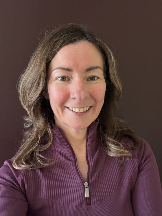 Lynette Tidy, smiling, wearing a purple zip-neck top