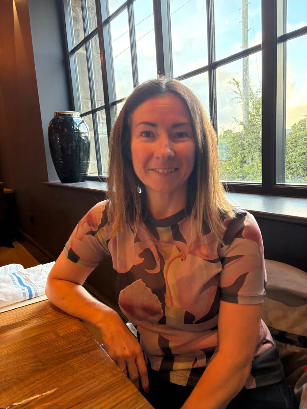 Lynette Tidy smiling, seated at a table by a large window