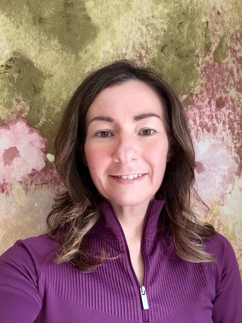 Lynette Tidy smiling, wearing a purple zip-neck top
