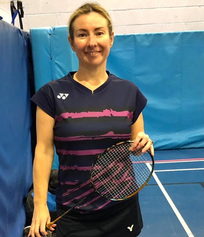 Lynette Tidy smiling in a navy badminton top, holding a racket